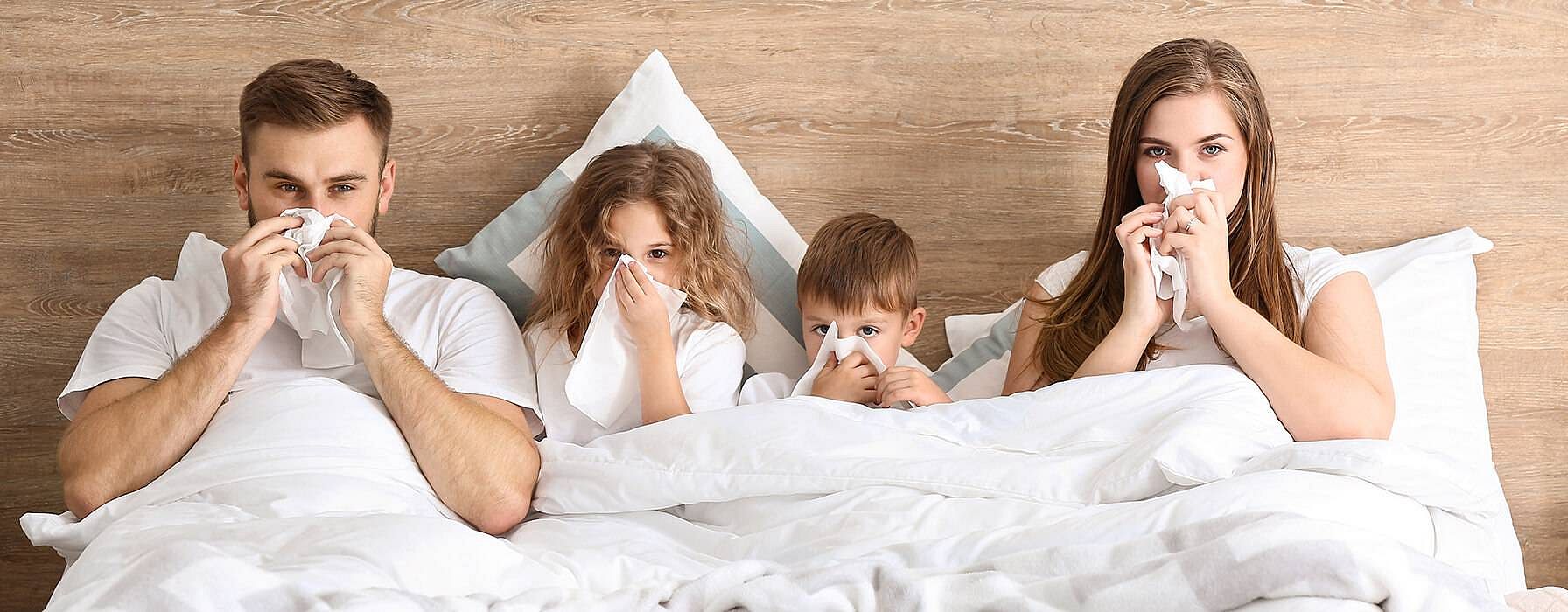 Familie im Bett alle schneuzen sich